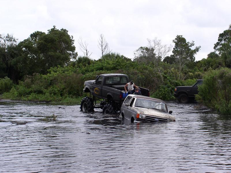 1991 Ford Bronco partially submerged in water next to a monster truck