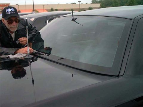 2000 Ford Crown Victoria - A man inspects the hood of a black 2000 Ford Crown Victoria, with another car visible in the background.