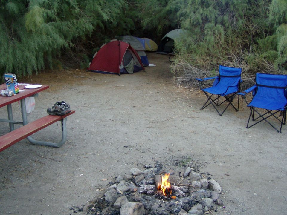 Tents, blue folding chairs and a campfire at a desert campsite