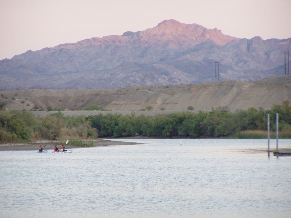 Two kayakers paddling on a river below desert mountains