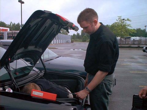 2000 Ford Crown Victoria - A man works on the trunk of a dark green 2000 Ford Crown Victoria, with another vehicle partially visible.
