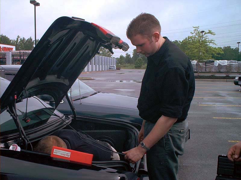 Dark green 2000 Ford Crown Victoria, trunk open, man working inside, another car visible behind