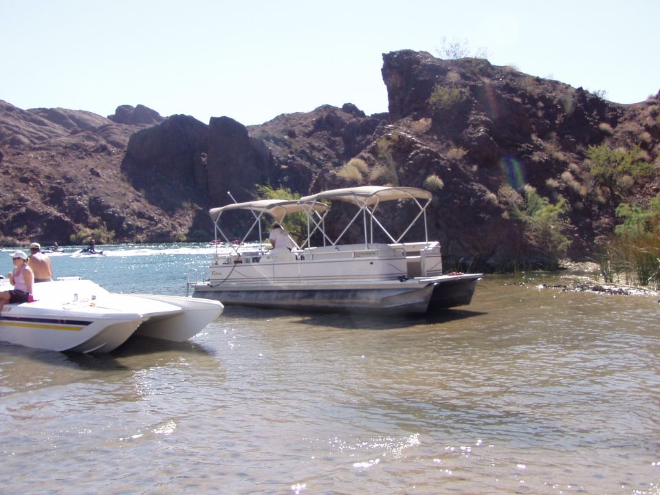 Tan pontoon boat and small powerboat beached at a desert river cove