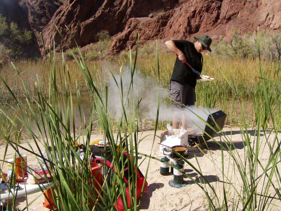 Man cooking on a portable stove at a riverside desert campsite