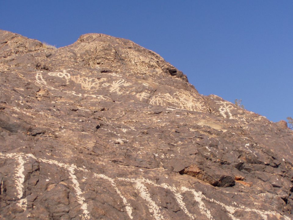 Petroglyphs on a dark desert hillside under a blue sky