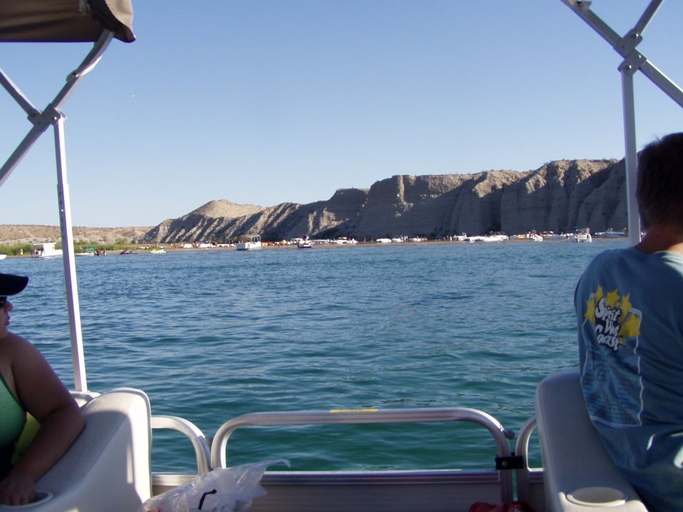 View from a pontoon boat of a lake with rocky bluffs and distant boats