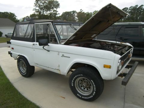 1974 Ford Bronco - A white 1974 Ford Bronco is parked outside with its hood open, revealing the engine compartment.