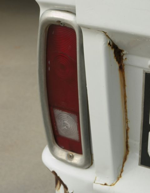 1974 Ford Bronco - Close-up of a white vehicle's rear corner, showing a red tail light and extensive rust along the body panel.