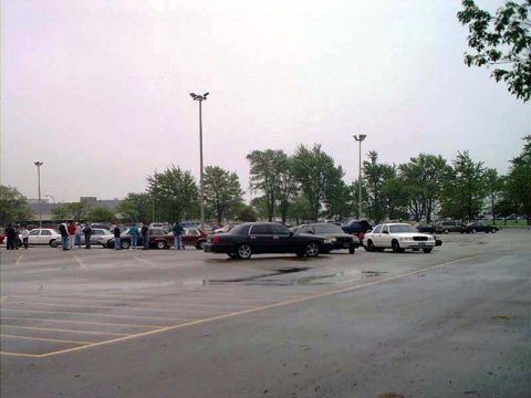 2000 Ford Crown Victoria - A group of people stand around in a parking lot with several vehicles visible.