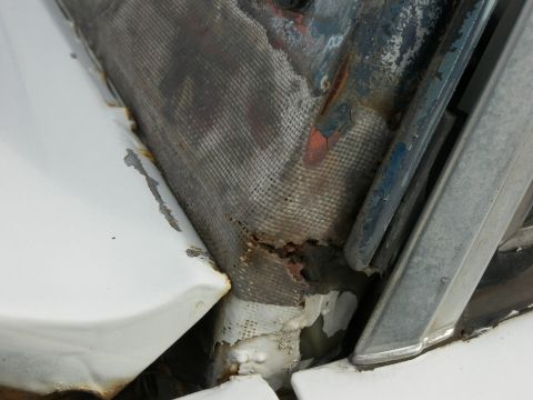 1974 Ford Bronco - The vehicle shows extensive rust and damage, particularly around a mesh-covered area near a metal trim piece.