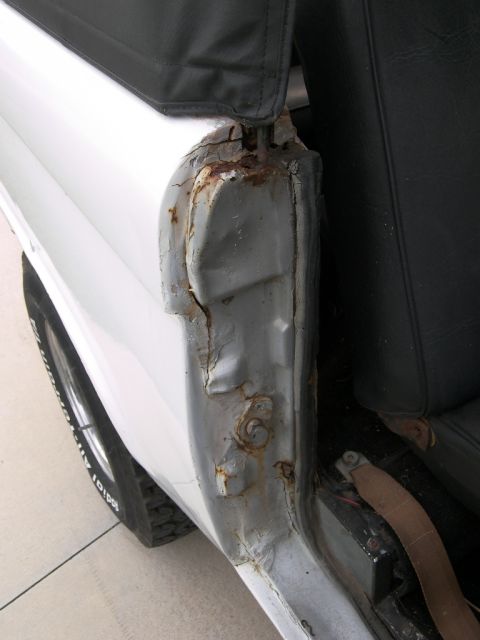 1974 Ford Bronco - Close-up view of significant rust damage on the door jamb of a white vehicle, revealing the underlying metal and interior components.