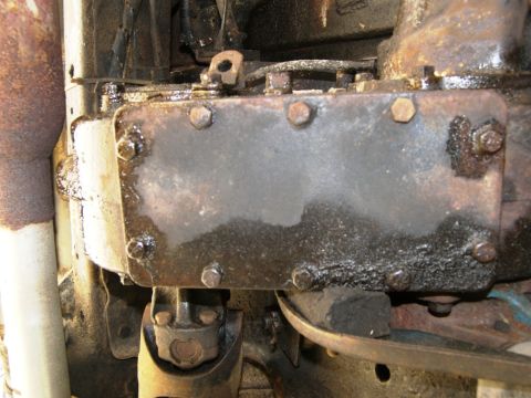 1974 Ford Bronco - Close-up view of a greasy drivetrain component, likely part of the transmission or transfer case, showing bolts and surface wear.