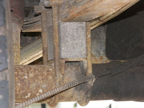 1974 Ford Bronco - The underside of a vehicle shows heavily rusted suspension parts, including leaf springs and U-bolts.