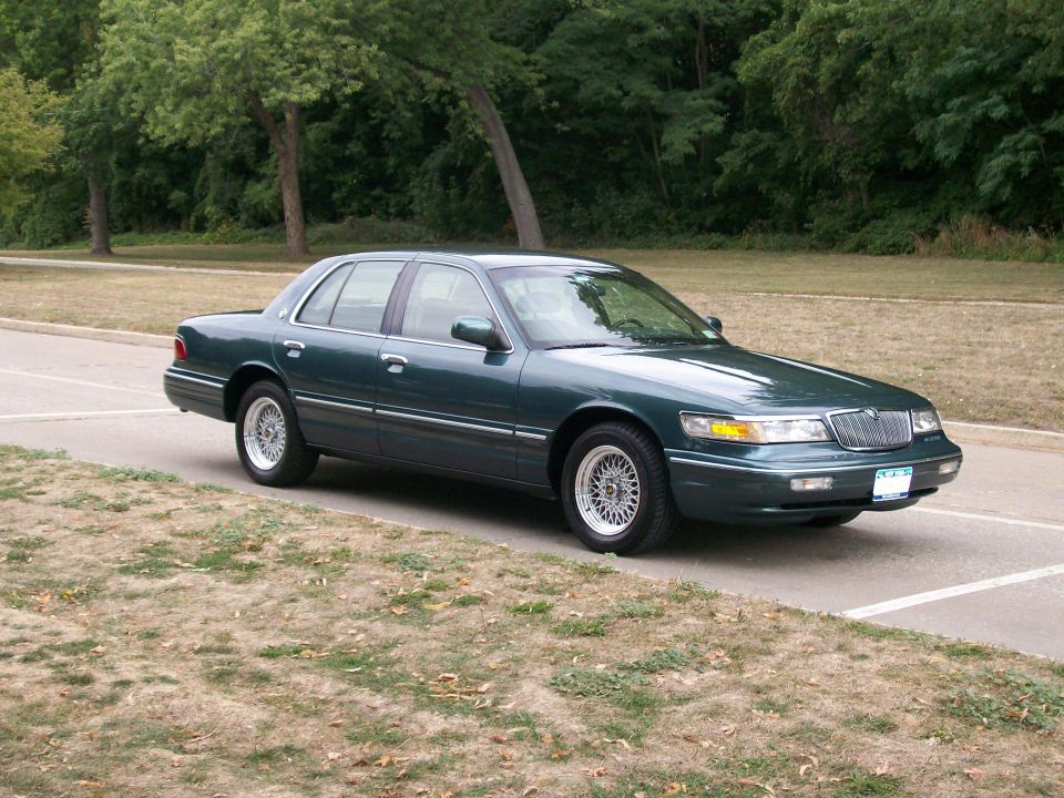 Dark green Mercury Grand Marquis sedan with chrome wheels parked on pavement near trees