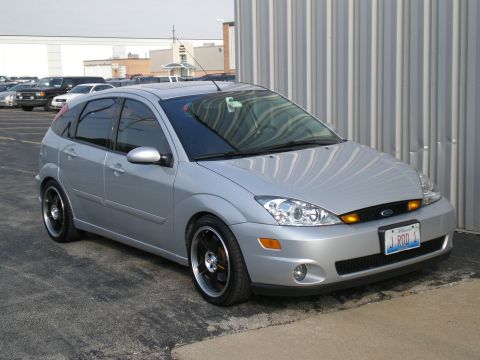 2003 Ford Focus - A silver 2003 Ford Focus hatchback is parked in front of a corrugated metal wall.