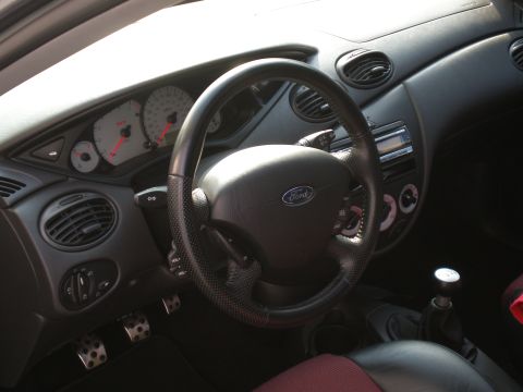 2003 Ford Focus - The interior of a 2003 Ford Focus, a black steering wheel and dashboard with white gauges.