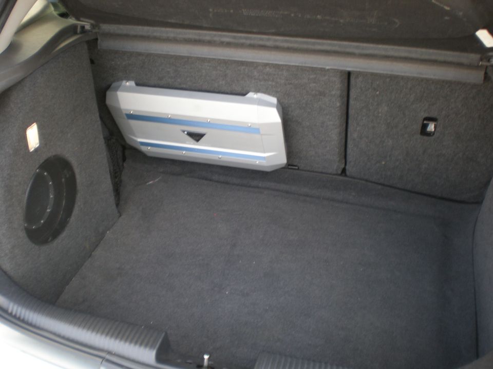 Car trunk with a subwoofer box on the left and a silver amplifier with blue stripes on the right