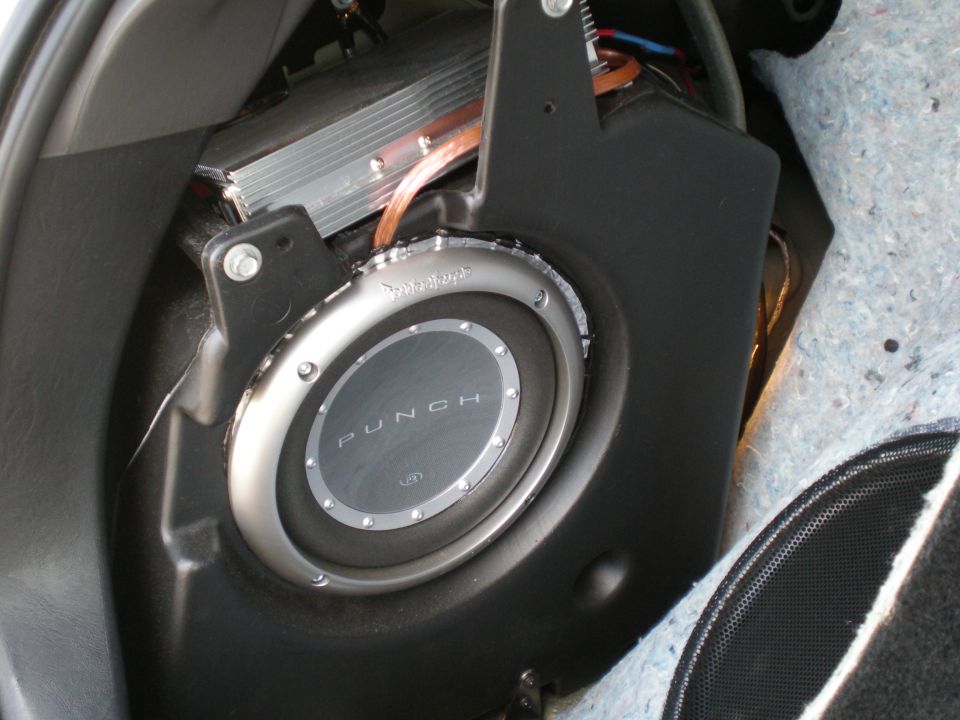 Subwoofer and amplifier installed in vehicle trunk, showing a Rockford Fosgate Punch subwoofer and silver amplifier