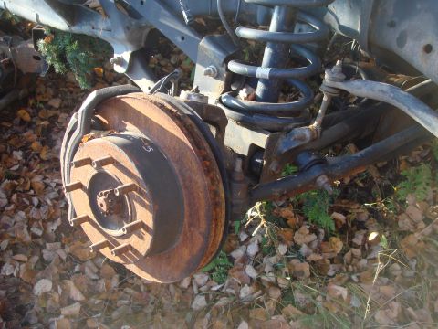 1996 Ford Bronco - Close-up of rusted vehicle brake rotor and suspension parts lying on the ground.
