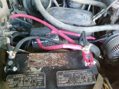 1995 Ford Bronco - Top-down engine-bay view of a black battery with DANGER/POISON warning labels on the case, fitted with new red positive and lead negative t…