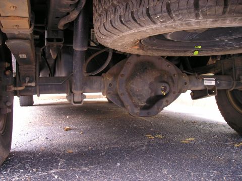 1989 Ford Bronco - Underbody view from behind a truck showing the rear axle housing and bolt-on differential cover, leaf springs, shock absorber and brake lin…