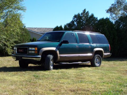 1995 Ford Bronco - This green GMC Suburban, likely from the mid-1990s, is seen parked on a grassy lawn under a clear blue sky.