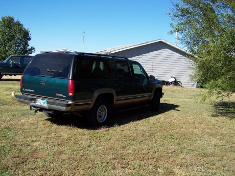 1995 Ford Bronco - A green GMC Suburban is parked in a yard with a building and another vehicle in the background.