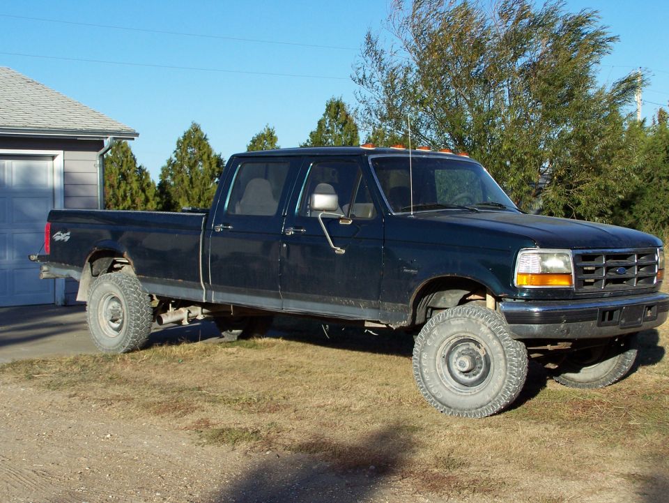 Dark blue 1992 Ford F-350 crew cab pickup truck, side view, parked on dry grass next to a garage