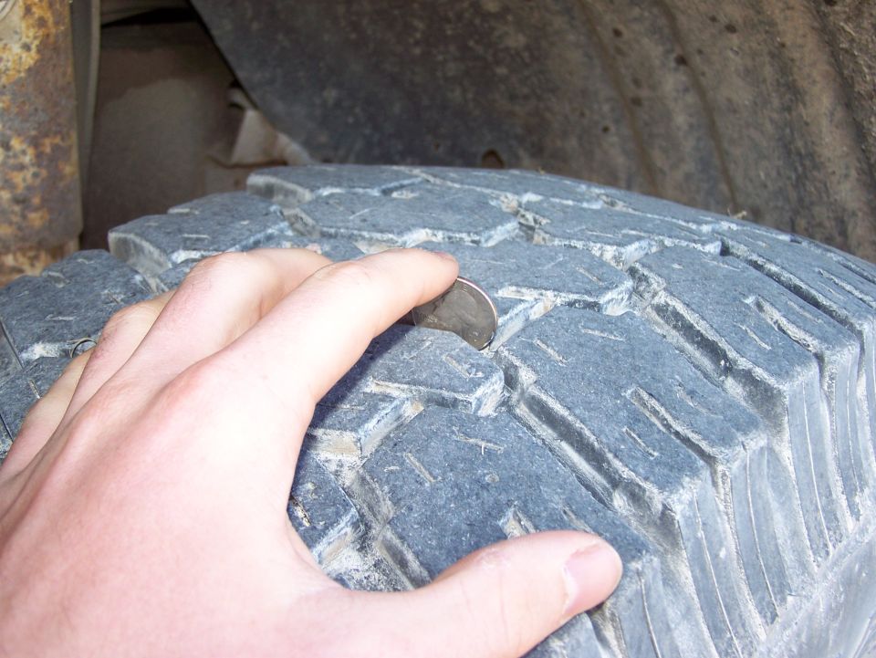 hand holding quarter on tire tread