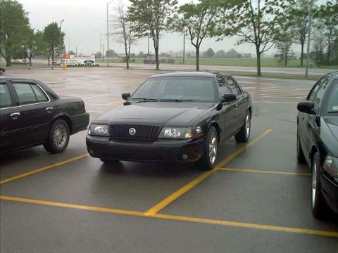 2000 Ford Crown Victoria - A black sedan is parked in a lot on a cloudy day.