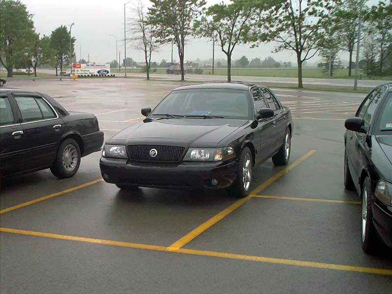 Black sedan parked in a lot, front 3/4 view. Visible grille and headlights