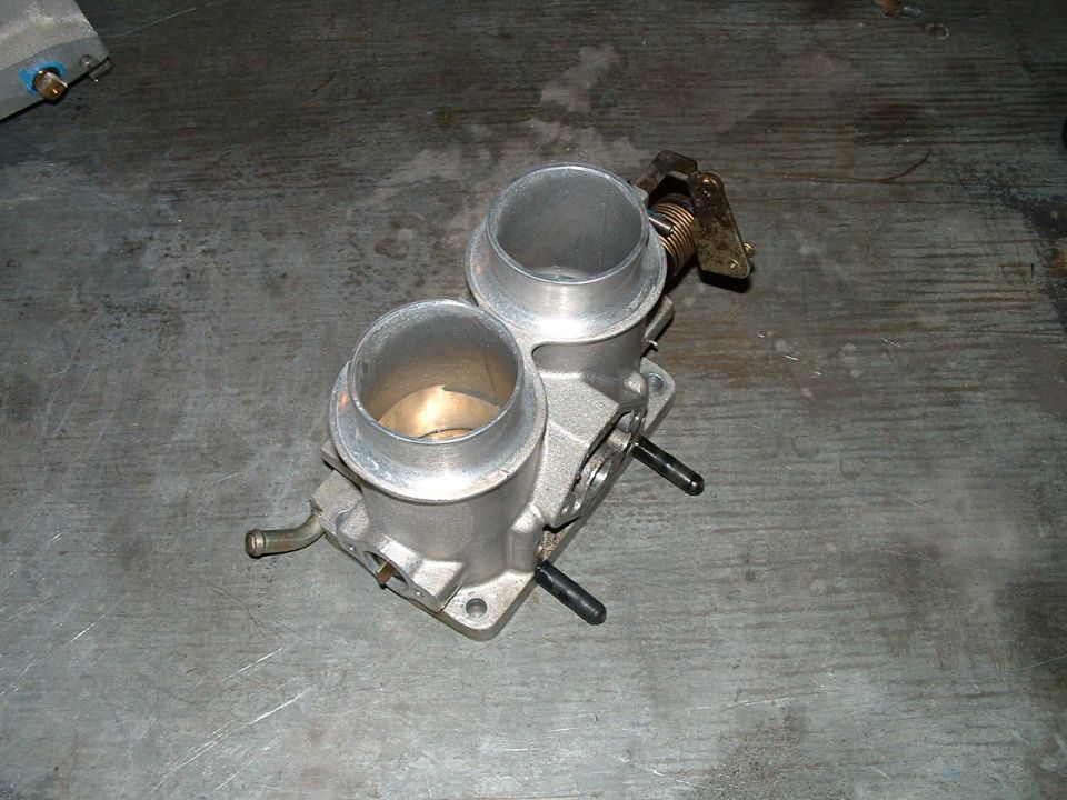 Dual throttle body assembly with linkage and springs, resting on a metal surface