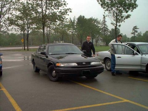 2000 Ford Crown Victoria - Two men stand near a black 2000 Ford Crown Victoria and a silver car in a parking lot.
