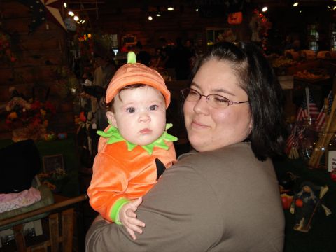 2000 Ford Crown Victoria - A woman holds a baby dressed in a pumpkin costume, likely during a fall festival or Halloween event.