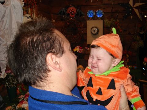 2000 Ford Crown Victoria - A man holds a baby dressed in a pumpkin costume, with the baby crying.