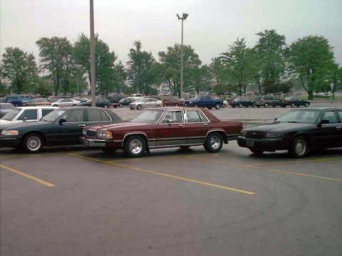 2000 Ford Crown Victoria - A maroon sedan is parked in a lot with other vehicles visible in the background.