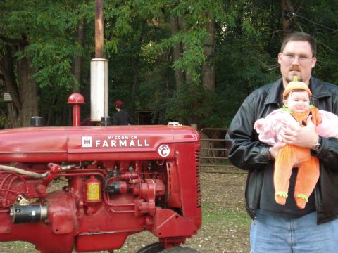 2000 Ford Crown Victoria - A man holds a baby dressed as a pumpkin next to a red McCormick Farmall tractor.