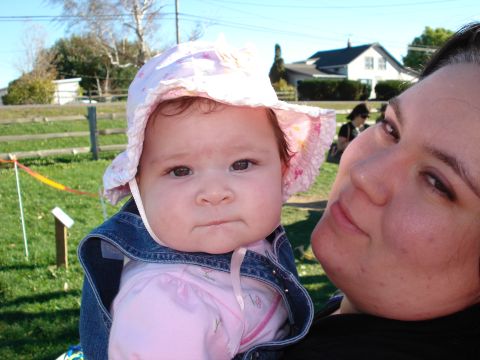2000 Ford Crown Victoria - A woman holds a baby in a sun hat and denim jacket in front of a house and fence.