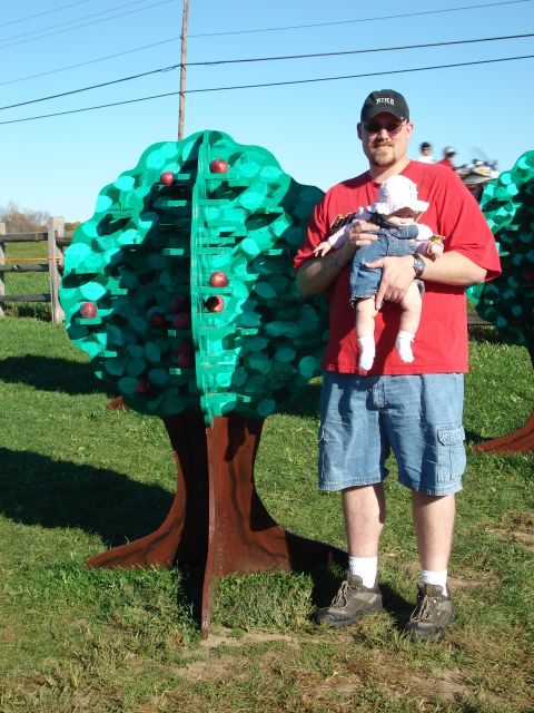 2000 Ford Crown Victoria - A man holds a baby while standing next to a large, decorative apple tree display.