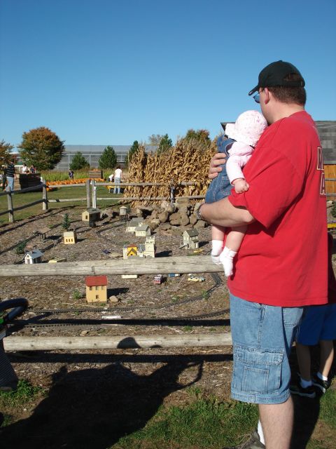 2000 Ford Crown Victoria - A man holds a baby while looking at a miniature town display at an outdoor event.