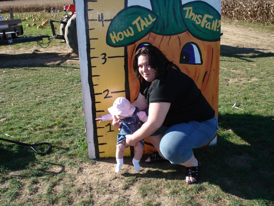 Woman holding baby next to a pumpkin-themed height chart that says "How Tall This Fall?"