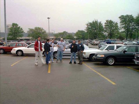 2000 Ford Crown Victoria - A group of men stand near a 2000 Ford Crown Victoria in a parking lot.