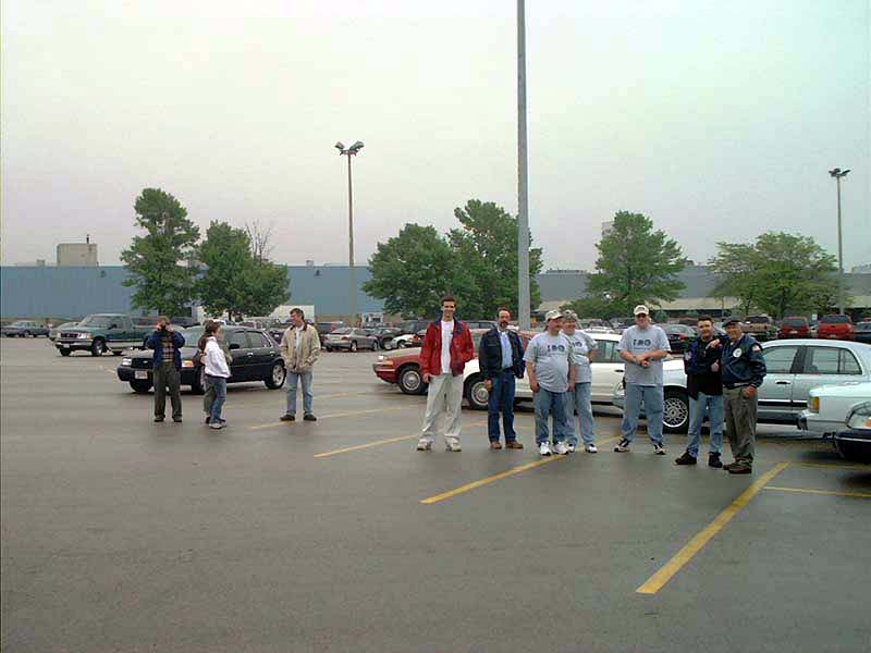 Group of people gathered in a parking lot with several cars visible