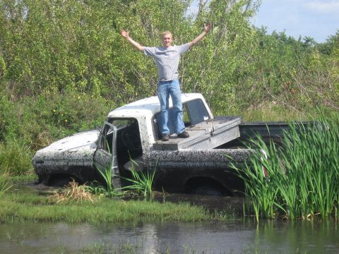 1979 Ford F-150 - A person stands triumphantly atop a mud-covered 1979 Ford F-150 stuck in a watery ditch.
