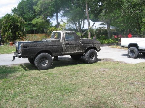 1979 Ford F-150 - Mud-covered 1979 Ford F-150 pickup truck parked on grass with another white truck in the background.