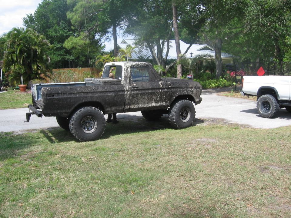 Mud-covered 1979 Ford F-150 pickup truck parked on grass, another white truck visible to the right