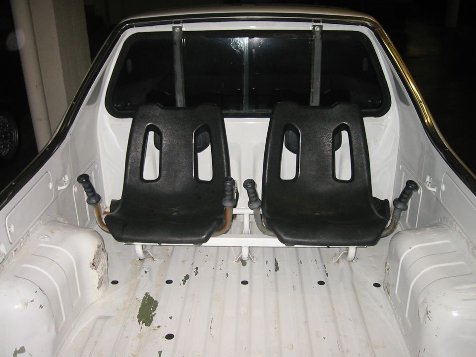 White Subaru Brat bed with two black rear-facing jump seats and grab handles mounted against the cab
