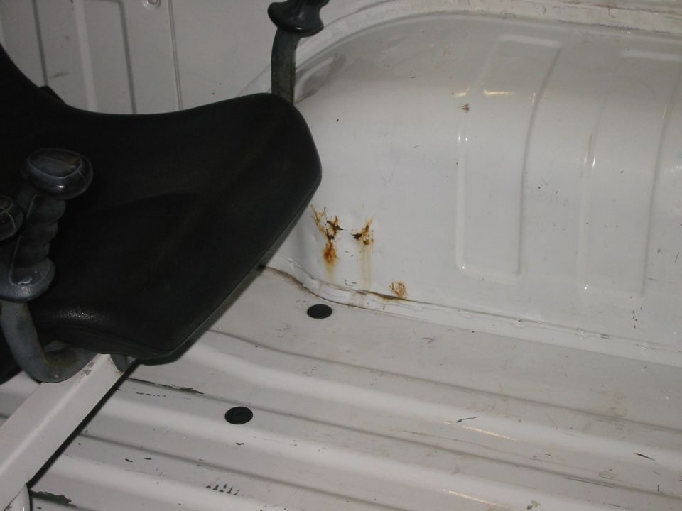 White truck bed with black bed-mounted jump seat and rust stains on the floor near a seam