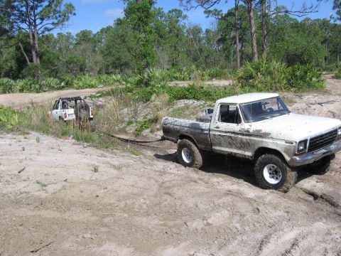 1979 Ford F-150 - A white 1979 Ford F-150 is stuck in the mud and being towed by another vehicle in an off-road scene.