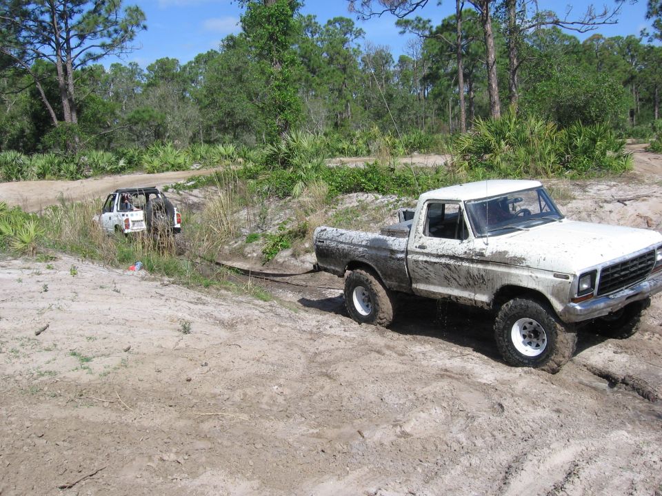 White 1979 Ford F-150 stuck in mud, being towed